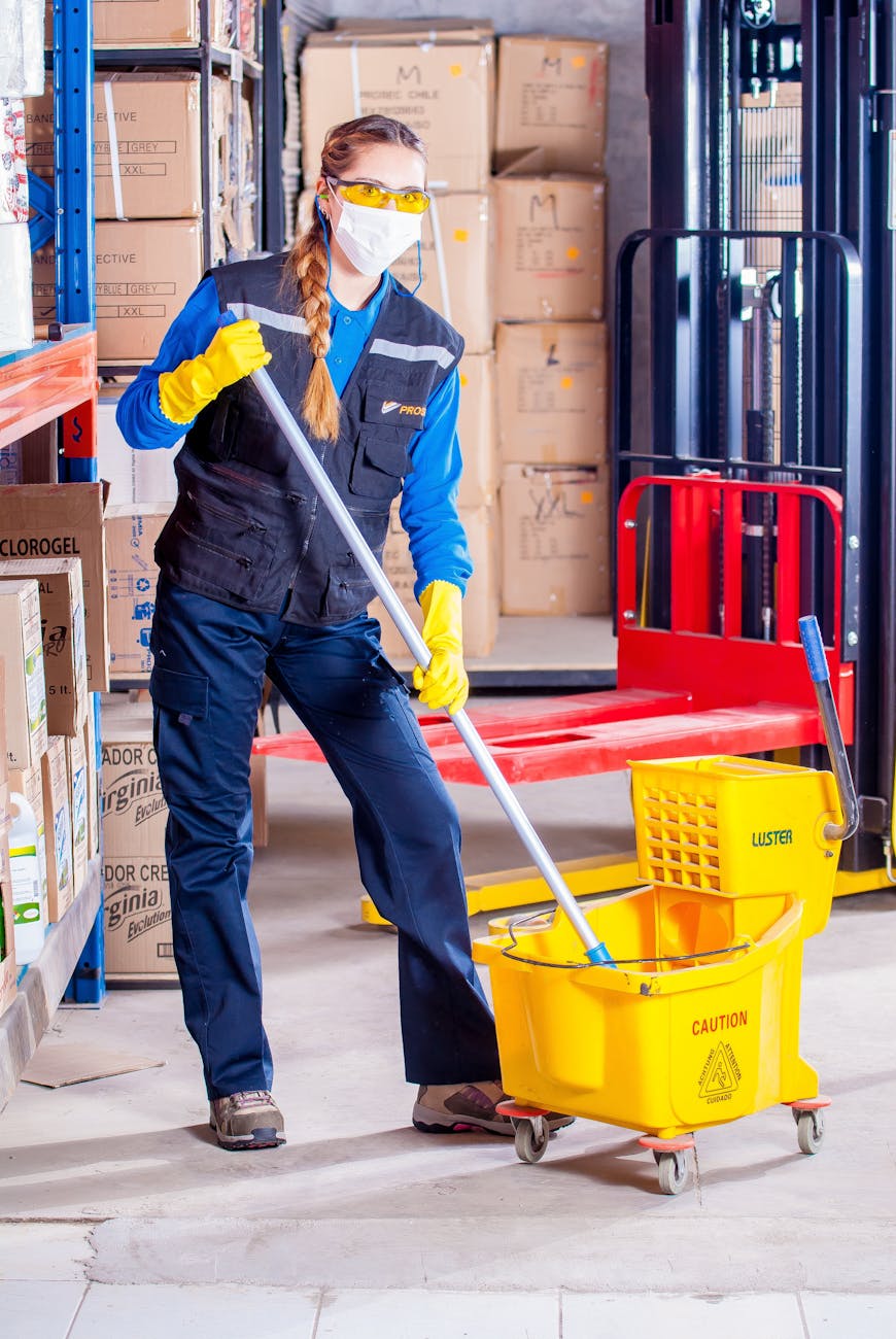 An adult cleaner with a mop and a mask on