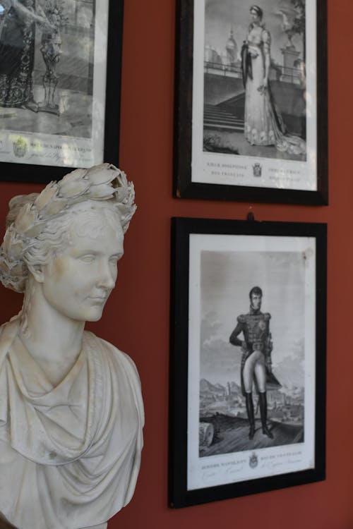 A bust of a man is displayed in front of framed pictures