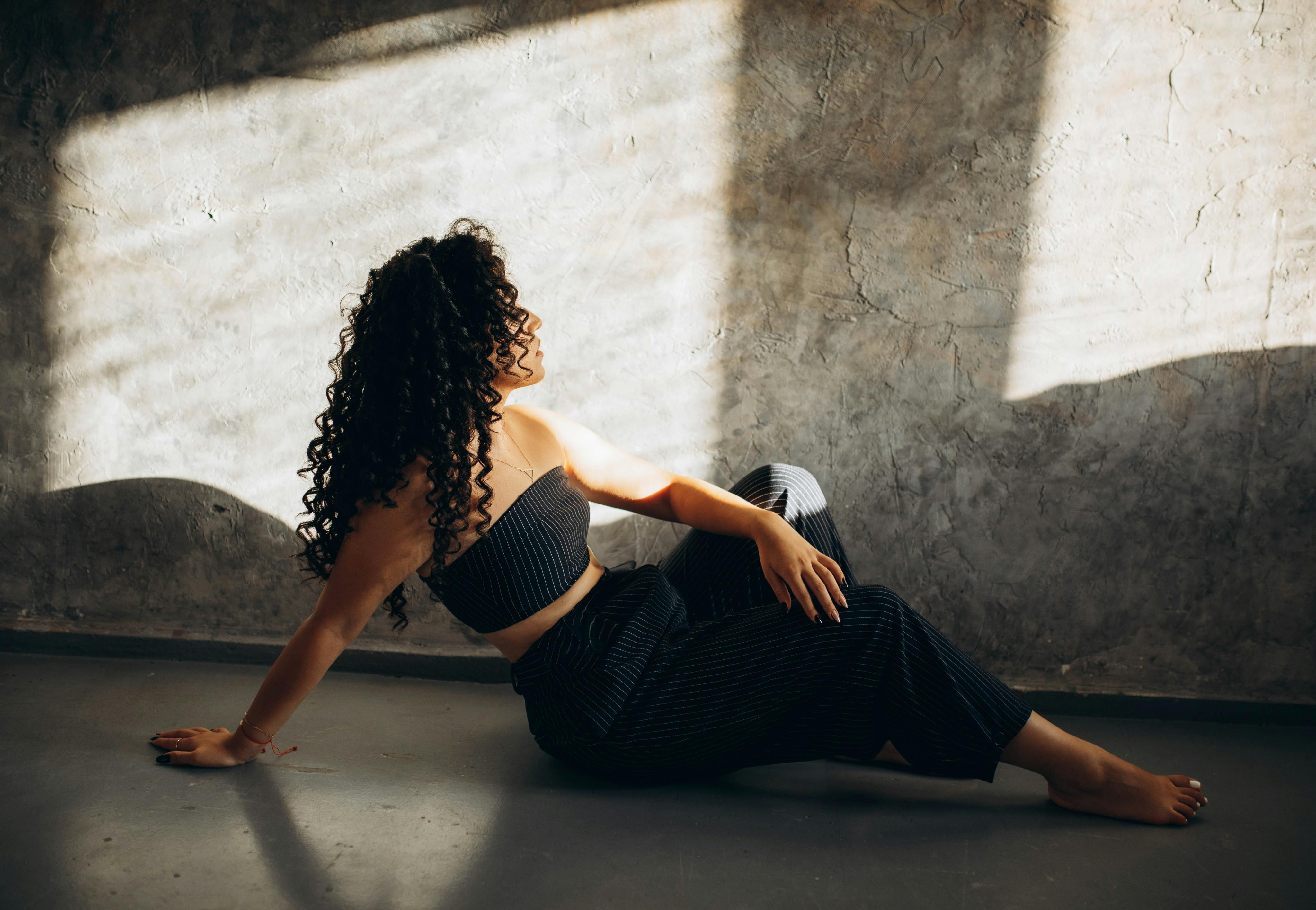 A stylish woman with curly hair sits gracefully in a well-lit room, showcasing casual fashion.