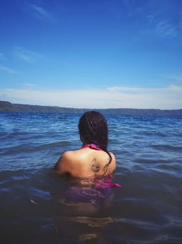 一个女人纹身后背的视角，在清澈的蓝天下于海洋中游泳