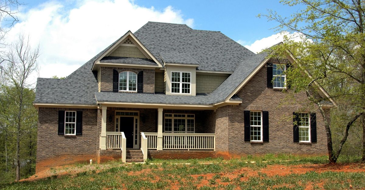 Classic two-story brick house with gable roof and front lawn in suburban setting.