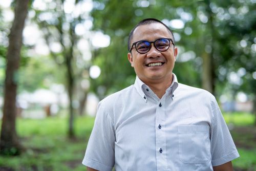 Free Portrait of a smiling Asian man with eyeglasses standing in a green park setting. Stock Photo