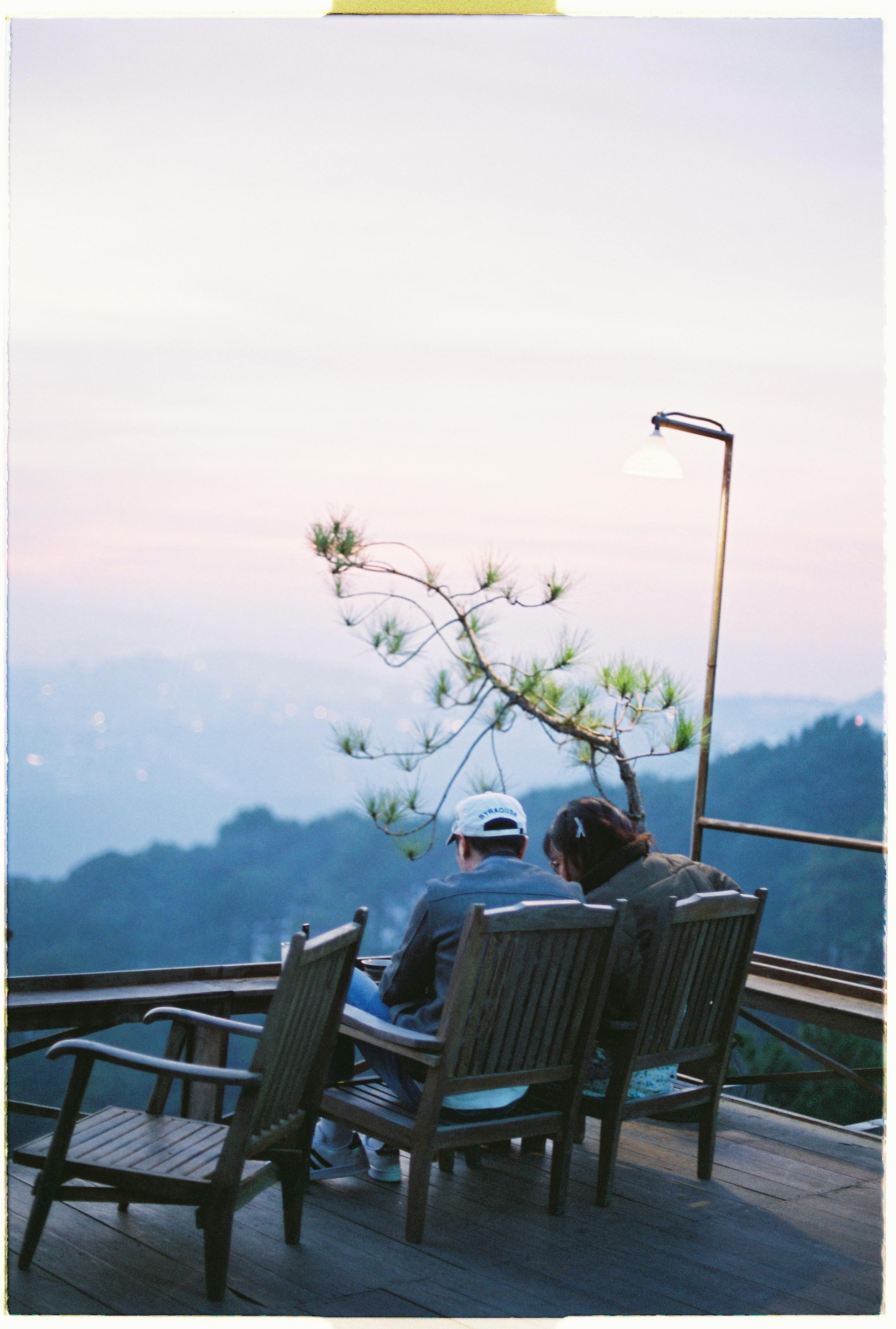 Couple seated on chairs enjoying a tranquil sunset view from a hilltop terrace.