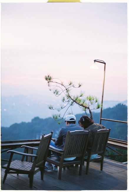 Couple seated on chairs enjoying a tranquil sunset view from a hilltop terrace.