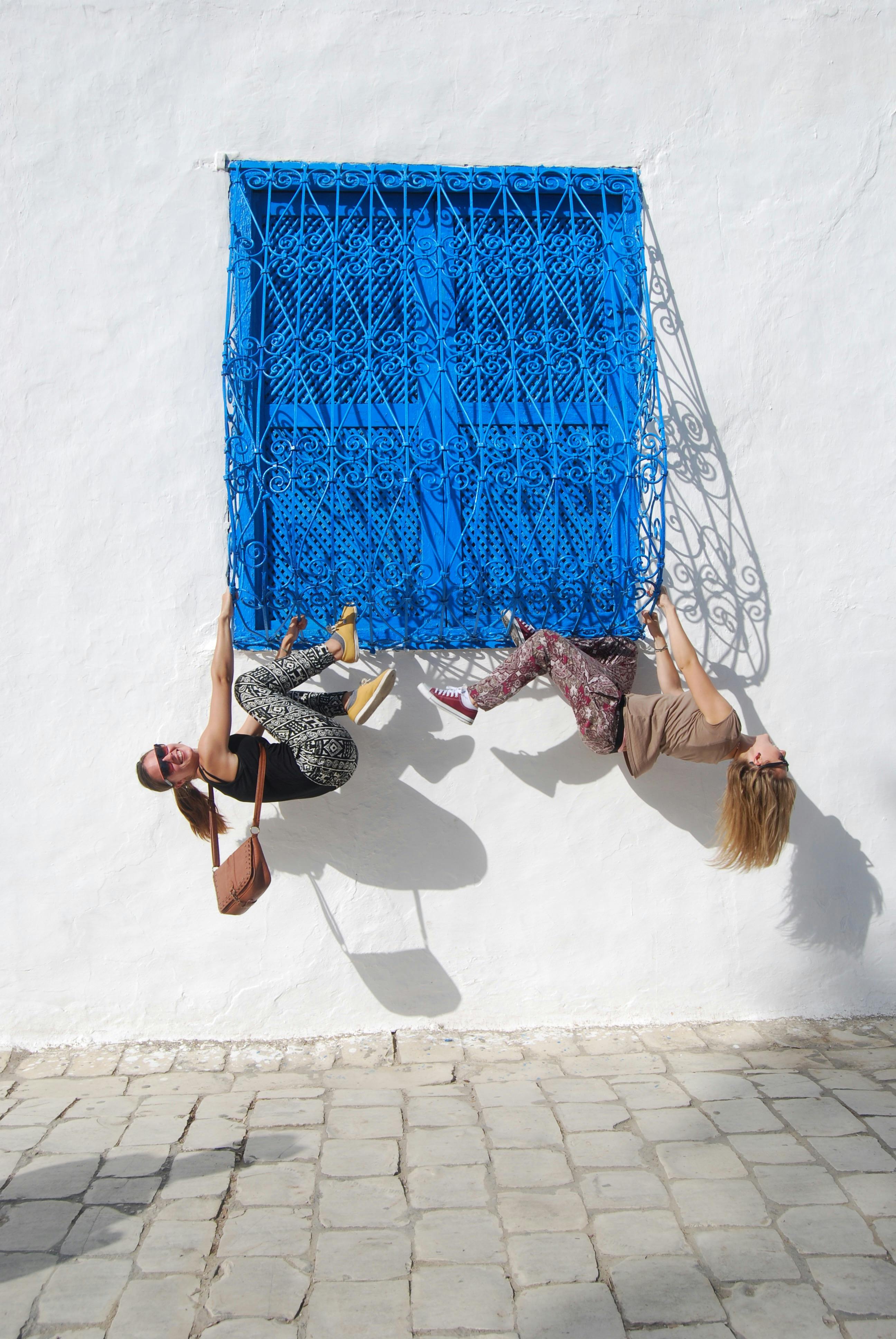 Two women in a lively street pose with vibrant blue window backdrop.