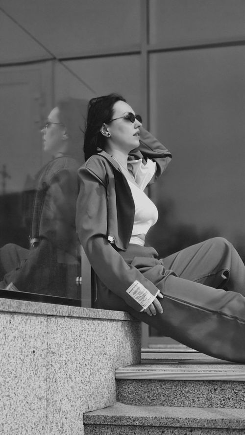 Free Stylish woman in sunglasses sitting by a reflective wall, capturing urban fashion vibes. Stock Photo