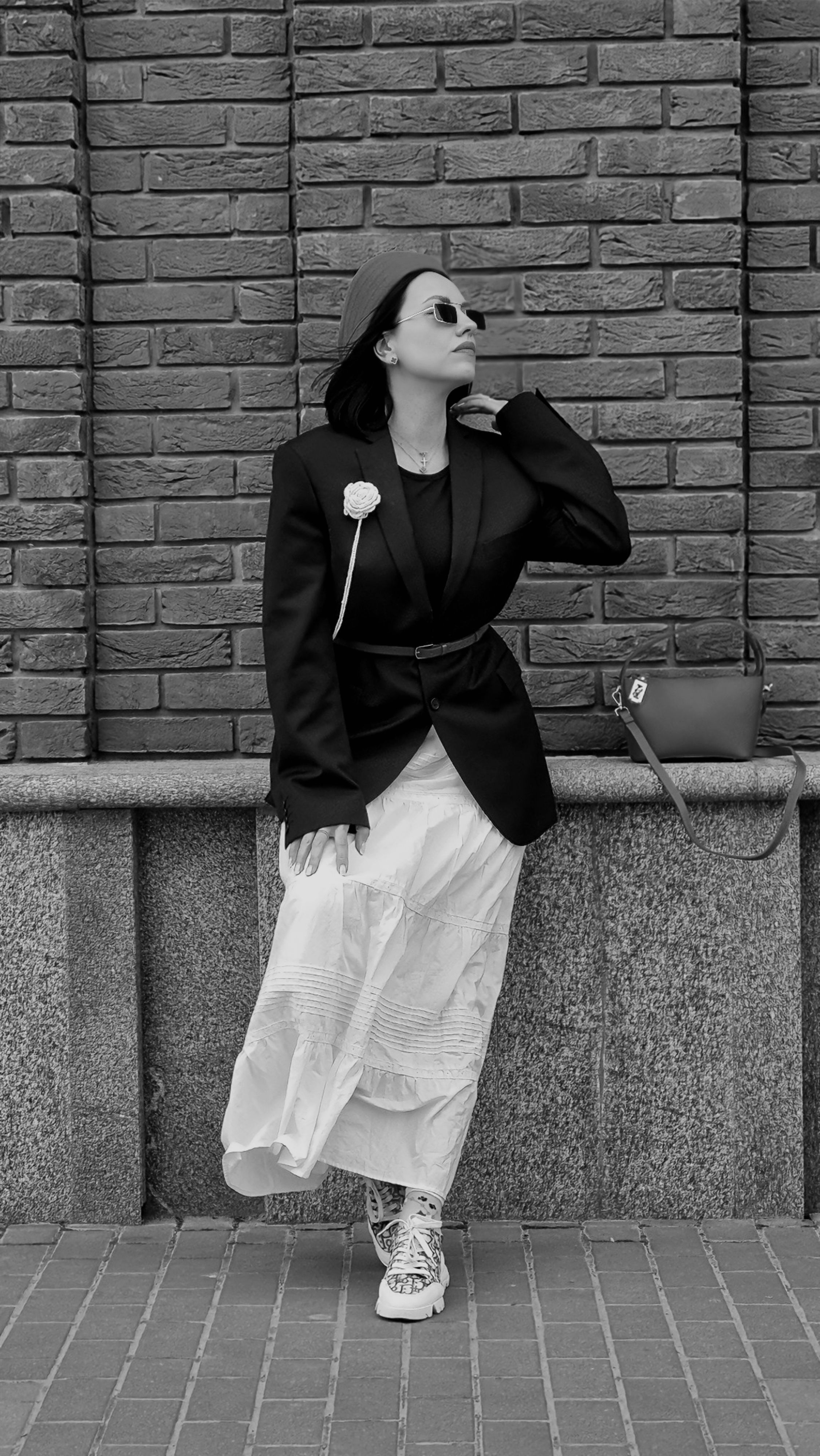 Stylish woman in blazer and dress posing outdoors in black and white