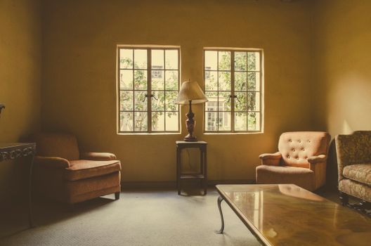 A vintage living room interior with armchairs and a lamp, filled with warm natural light.