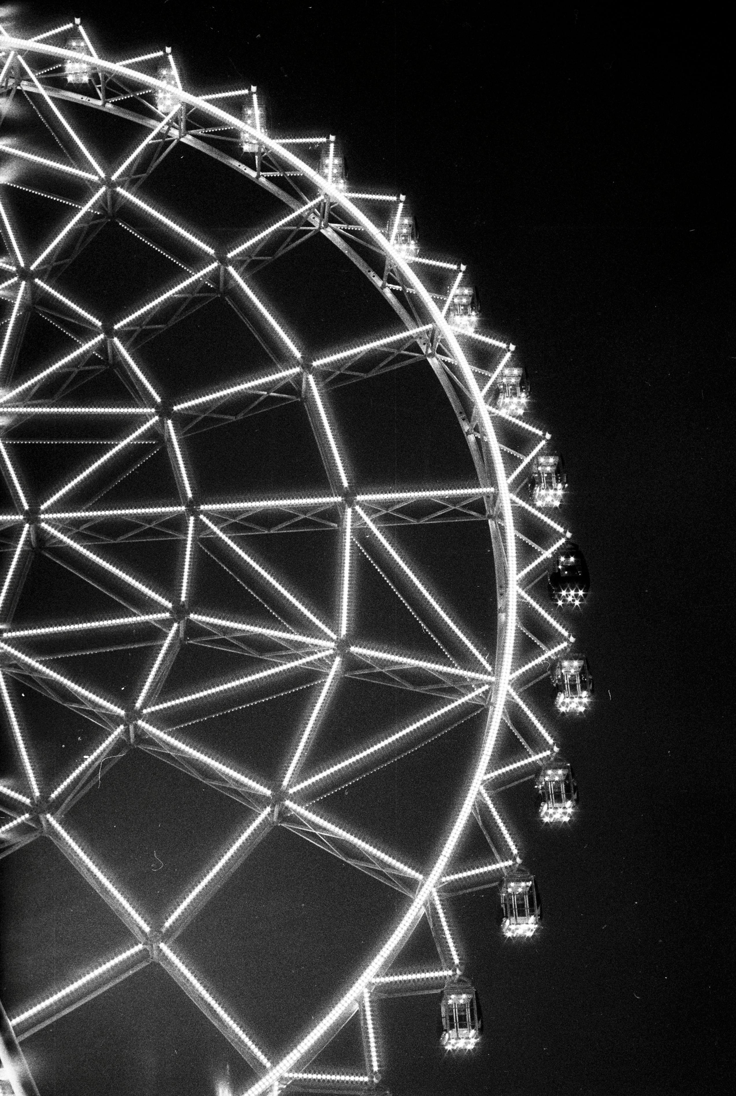 A black and white photo of a glowing Ferris wheel at night, showcasing illuminated gondolas.