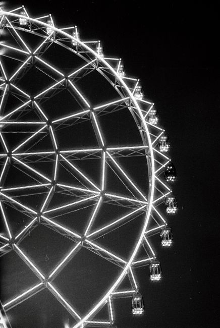 A black and white photo of a glowing Ferris wheel at night, showcasing illuminated gondolas.