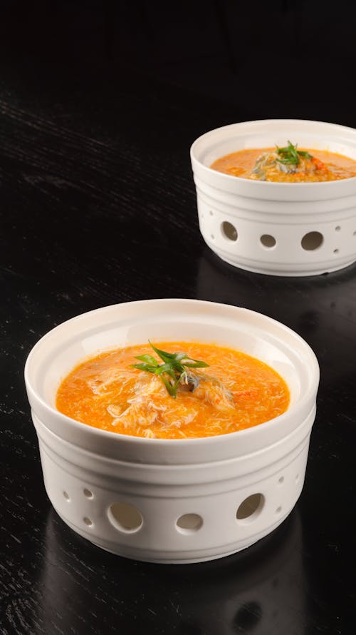 Two bowls of soup with garnish on a table