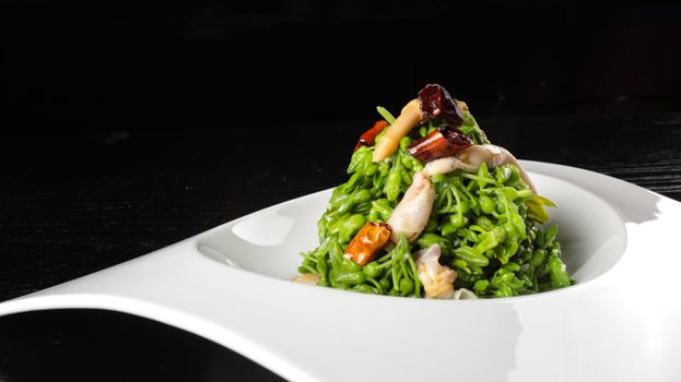 Close-up of a vibrant green pasta dish garnished with mushrooms, shot in a restaurant setting.