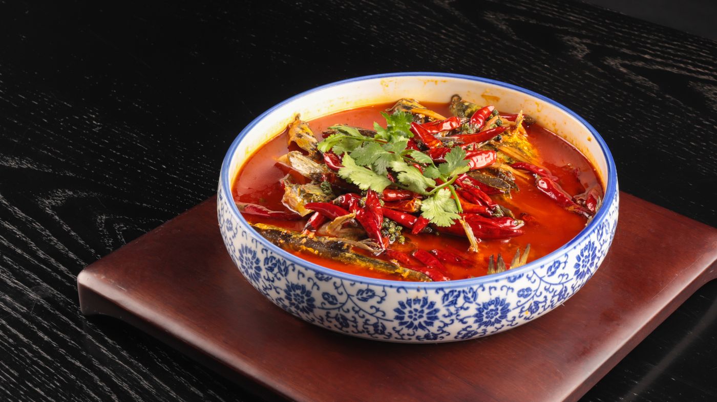 A vibrant bowl of spicy tomato soup garnished with herbs and peppers on a wooden board.