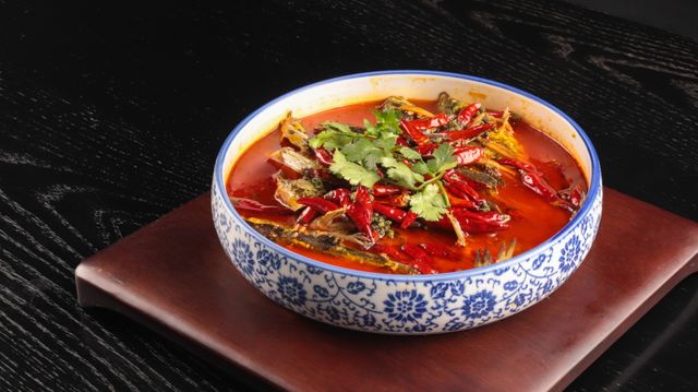 A vibrant bowl of spicy tomato soup garnished with herbs and peppers on a wooden board.