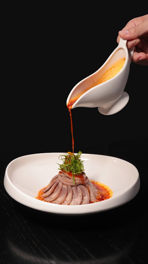 A person pouring sauce on a dish of meat