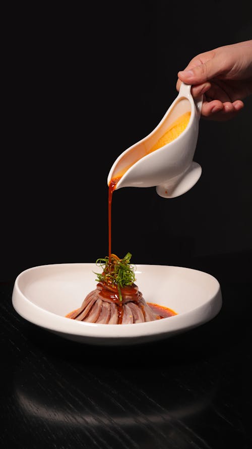 A person pouring sauce on a plate with food