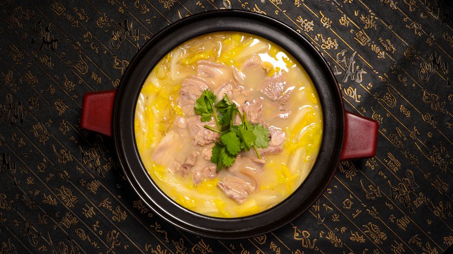Top view of a delicious traditional meat stew garnished with herbs, served in a black ceramic pot