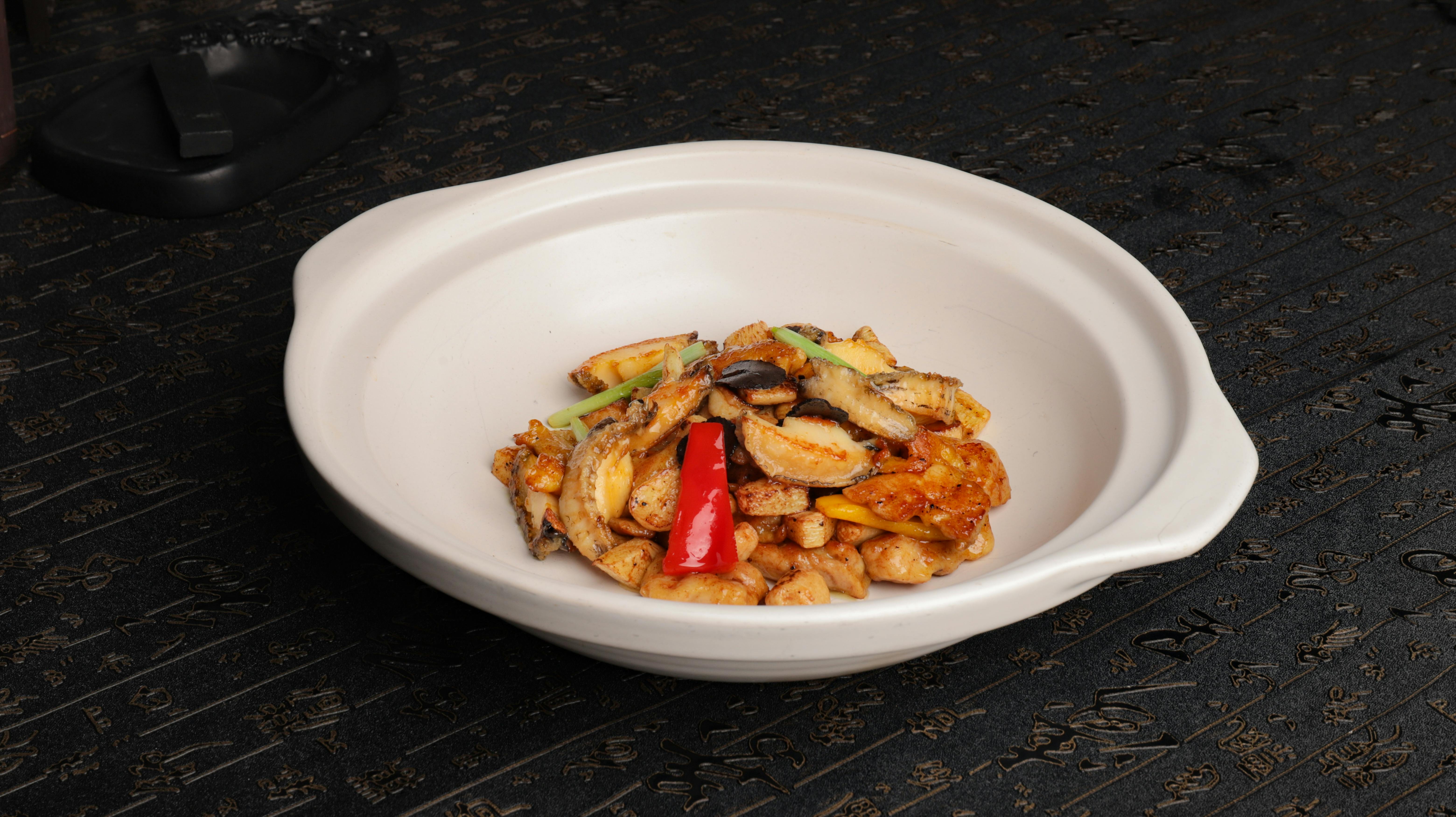 A close-up of a vibrant Asian stir-fry dish served in a white ceramic bowl on a textured dark surface.