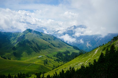 A view of a mountain range with green grass and clouds