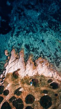 A stunning aerial shot of a rocky shoreline blending into clear turquoise waters, showcasing natural beauty.