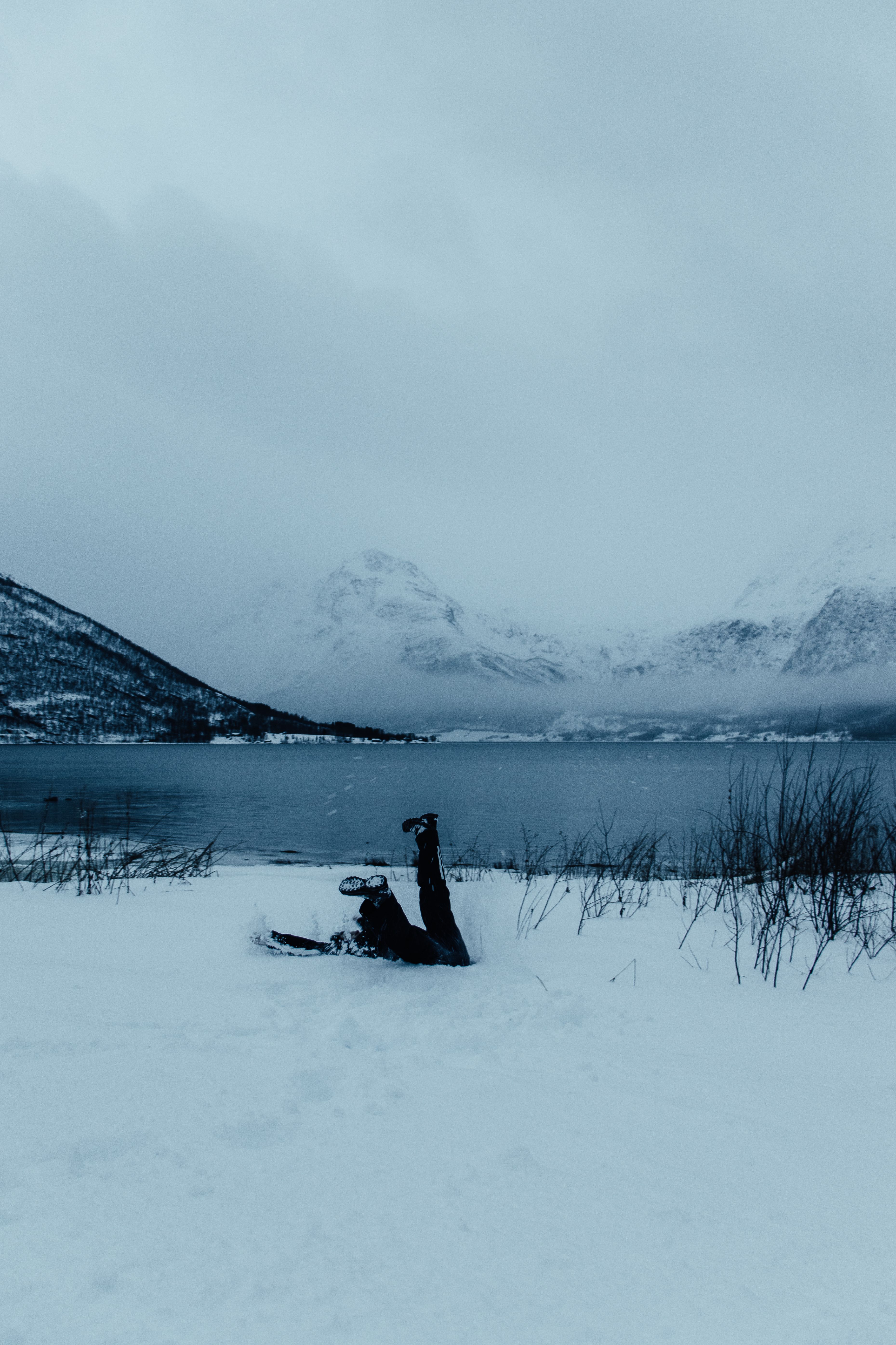 Person Lying Down in Snow near Lake in Winter · Free Stock Photo