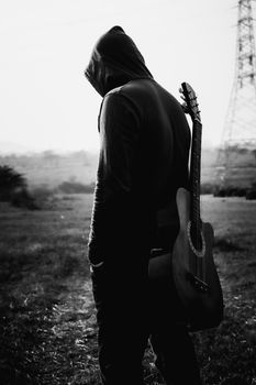 Silhouette of a hooded man with guitar in rural Pune, India.