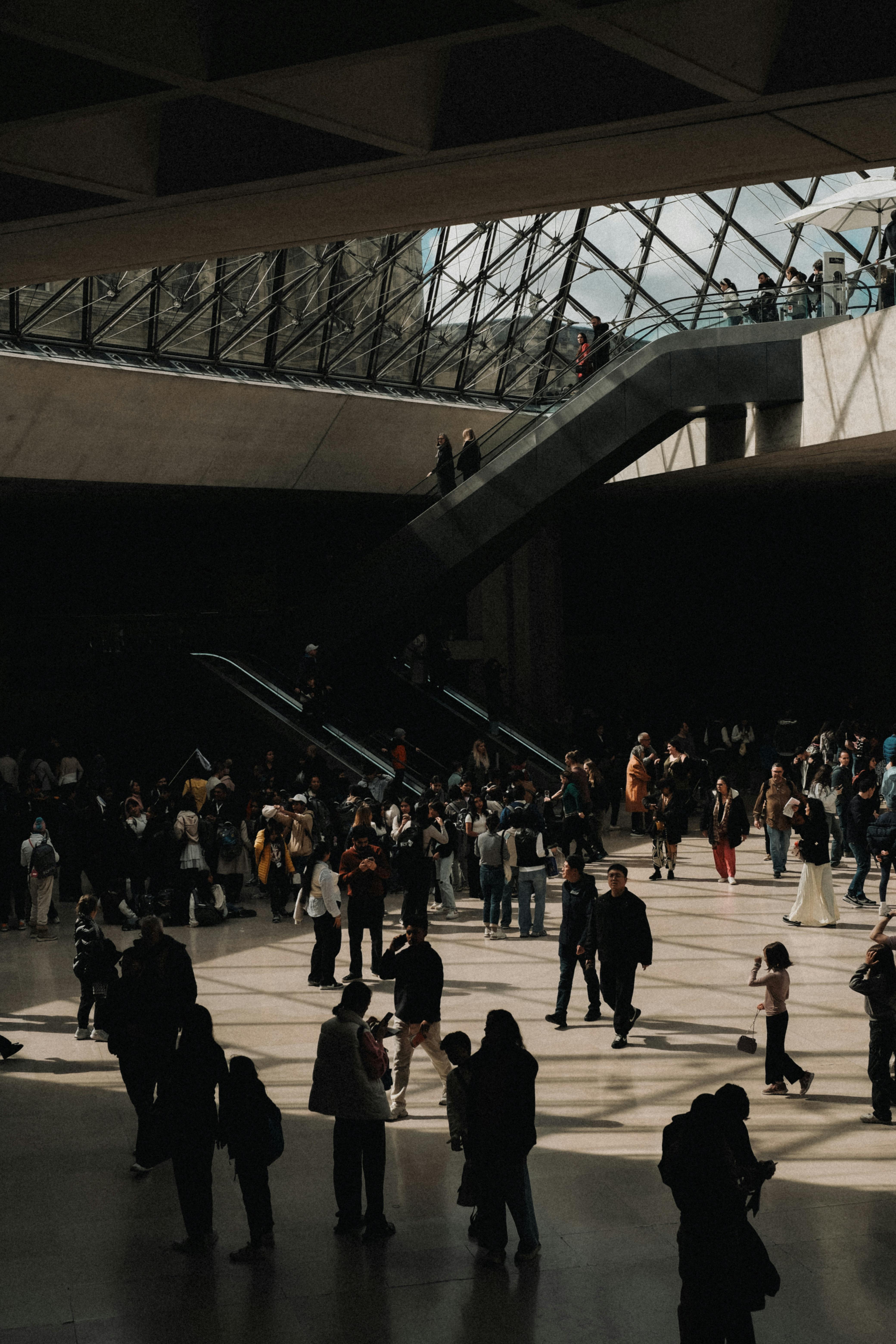 Crowd inside Louvre Pyramid entrance, Paris, capturing urban tourism vibes.