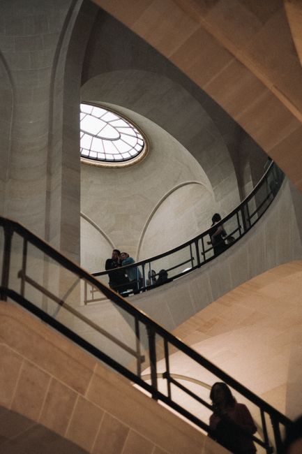Visitors explore the iconic architectural stairwell of the Louvre Museum in Paris.
