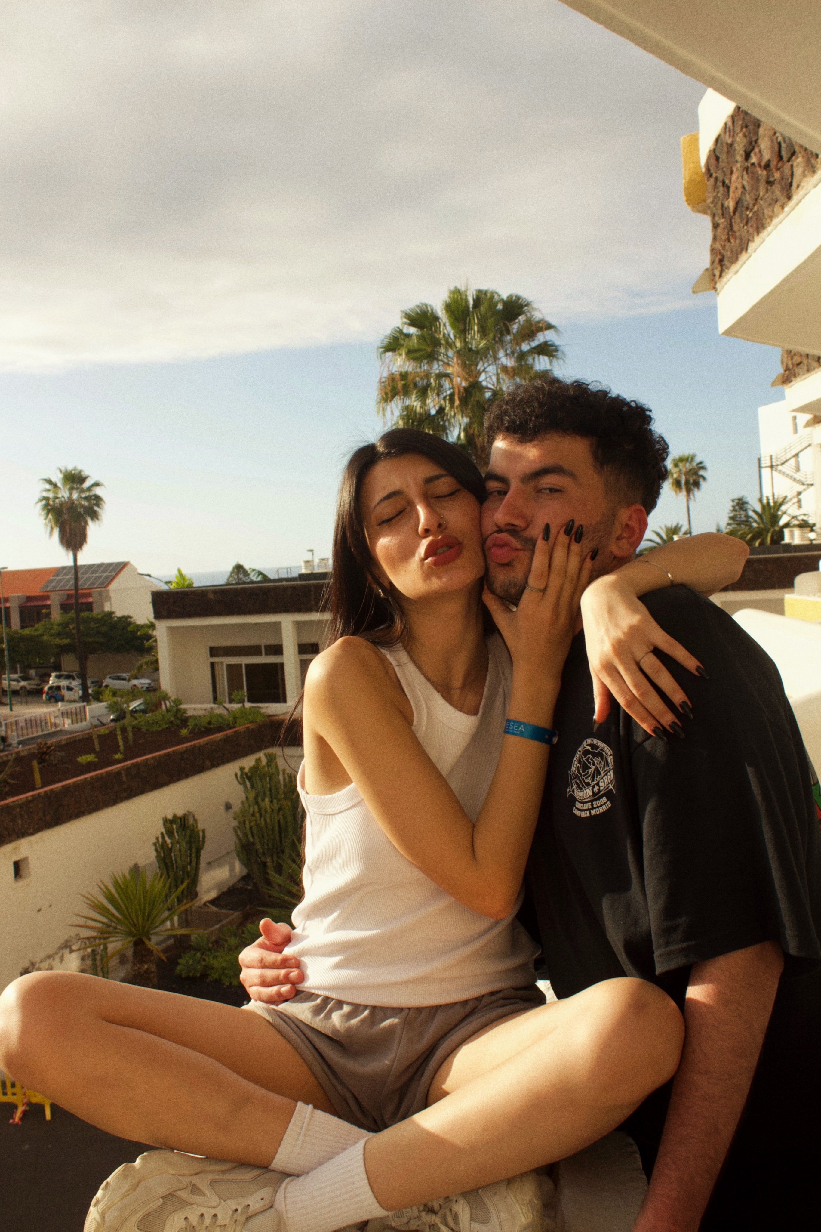 Affectionate young couple enjoying a sunny day on a Spanish balcony with palm trees in the background.