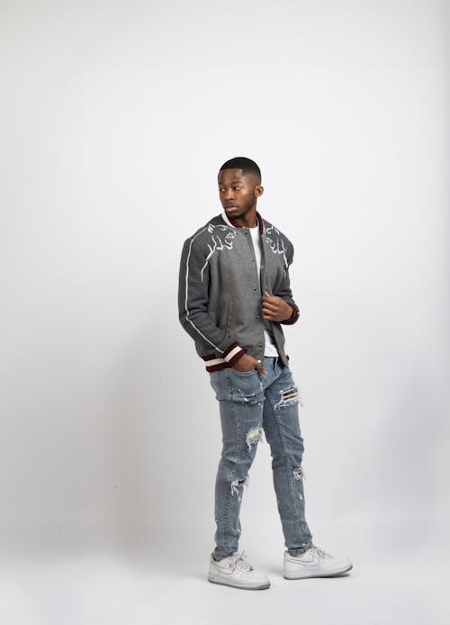 A man in a jacket and jeans standing in front of a white background
