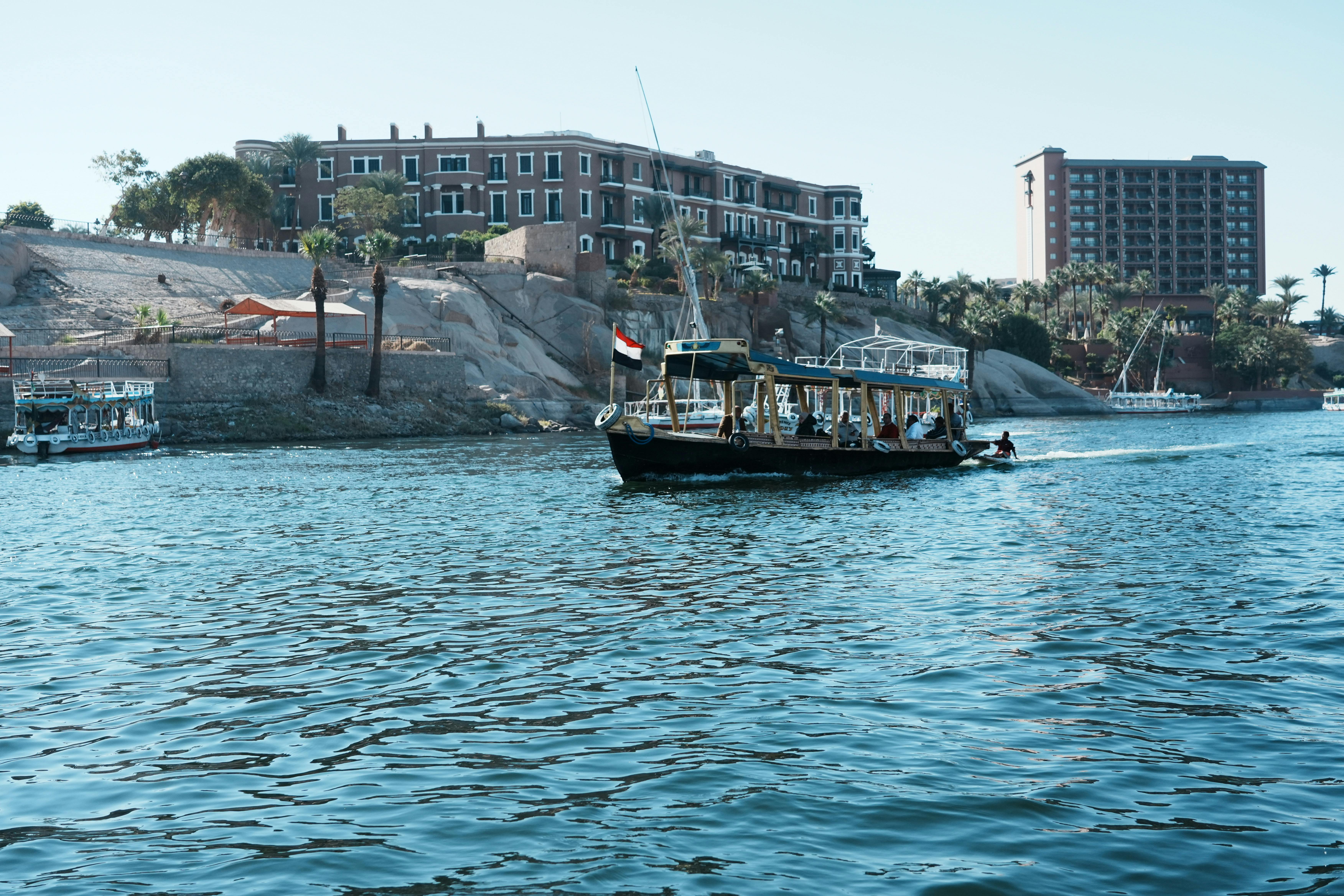 Scenic view of tour boats navigating the Nile River with architectural backdrop in Aswan, Egypt.
