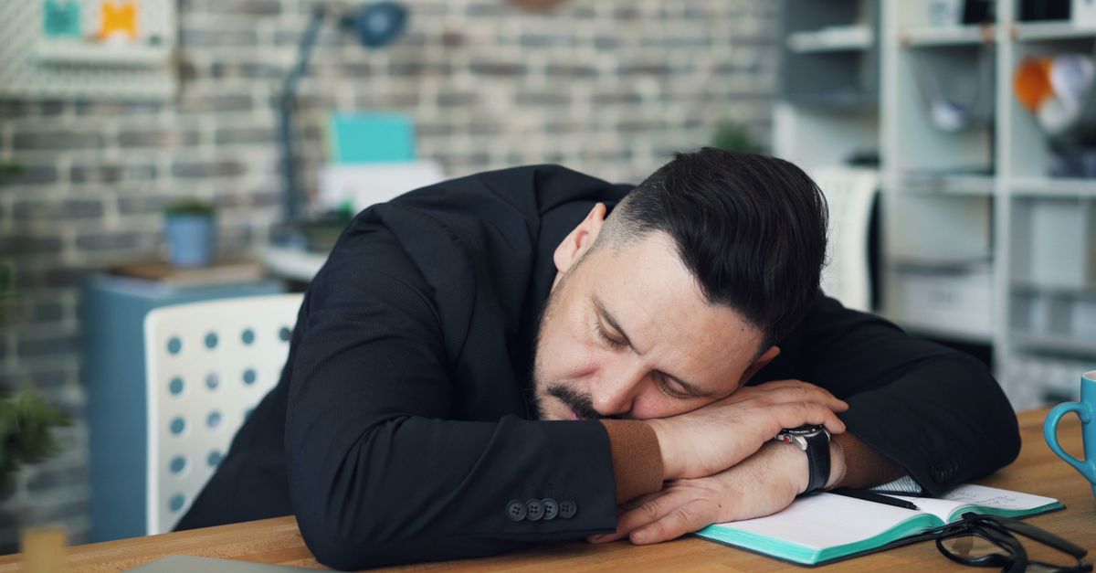Exhausted man in office resting on desk with notebook and coffee mug. - Evidence evidence guide for caffeine sleep randomized trial