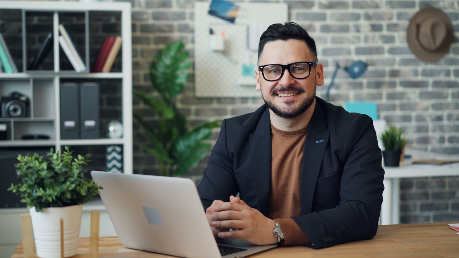 Businessman with eyeglasses smiling while working on a laptop in a modern office.