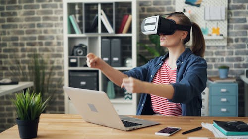 A woman wearing a virtual reality headset in front of a laptop
