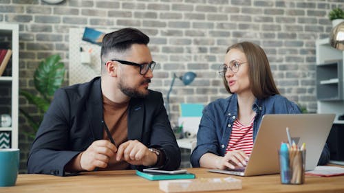 Two people sitting at a table with laptops