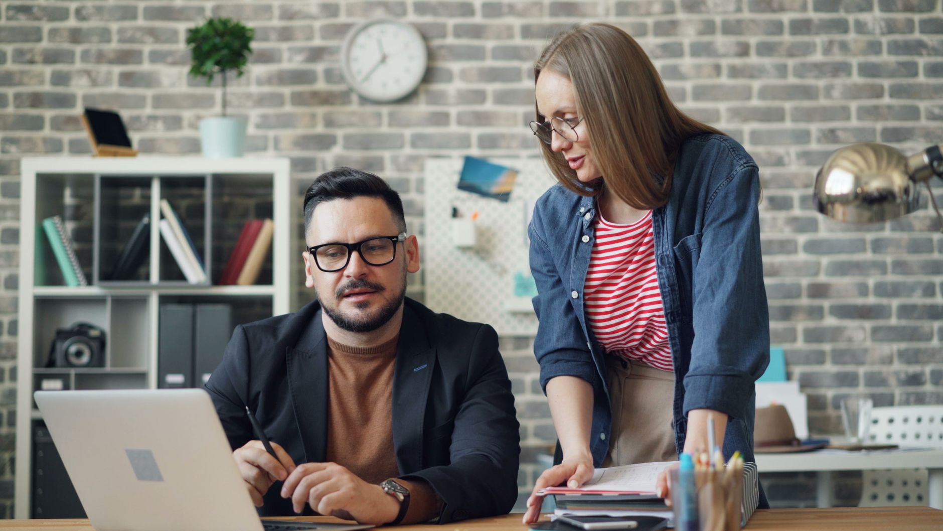 Two office coworkers engaged in a collaborative discussion at a modern office desk.