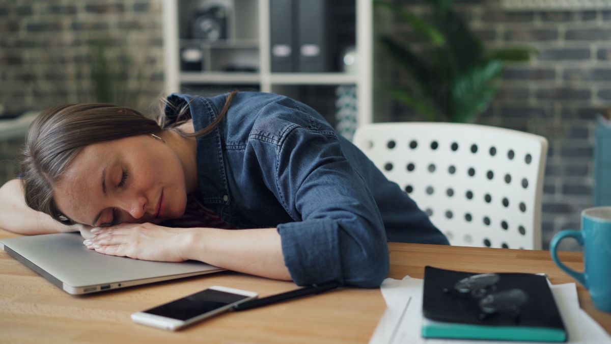 Mujer agotada dormida sobre el escritorio de su oficina por falta de energía