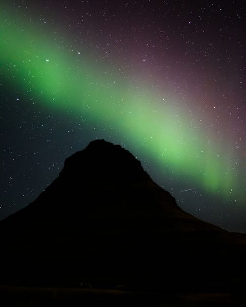 Free A breathtaking view of the Aurora Borealis illuminating the night sky over a mountain in Reykjavík, Iceland. Stock Photo