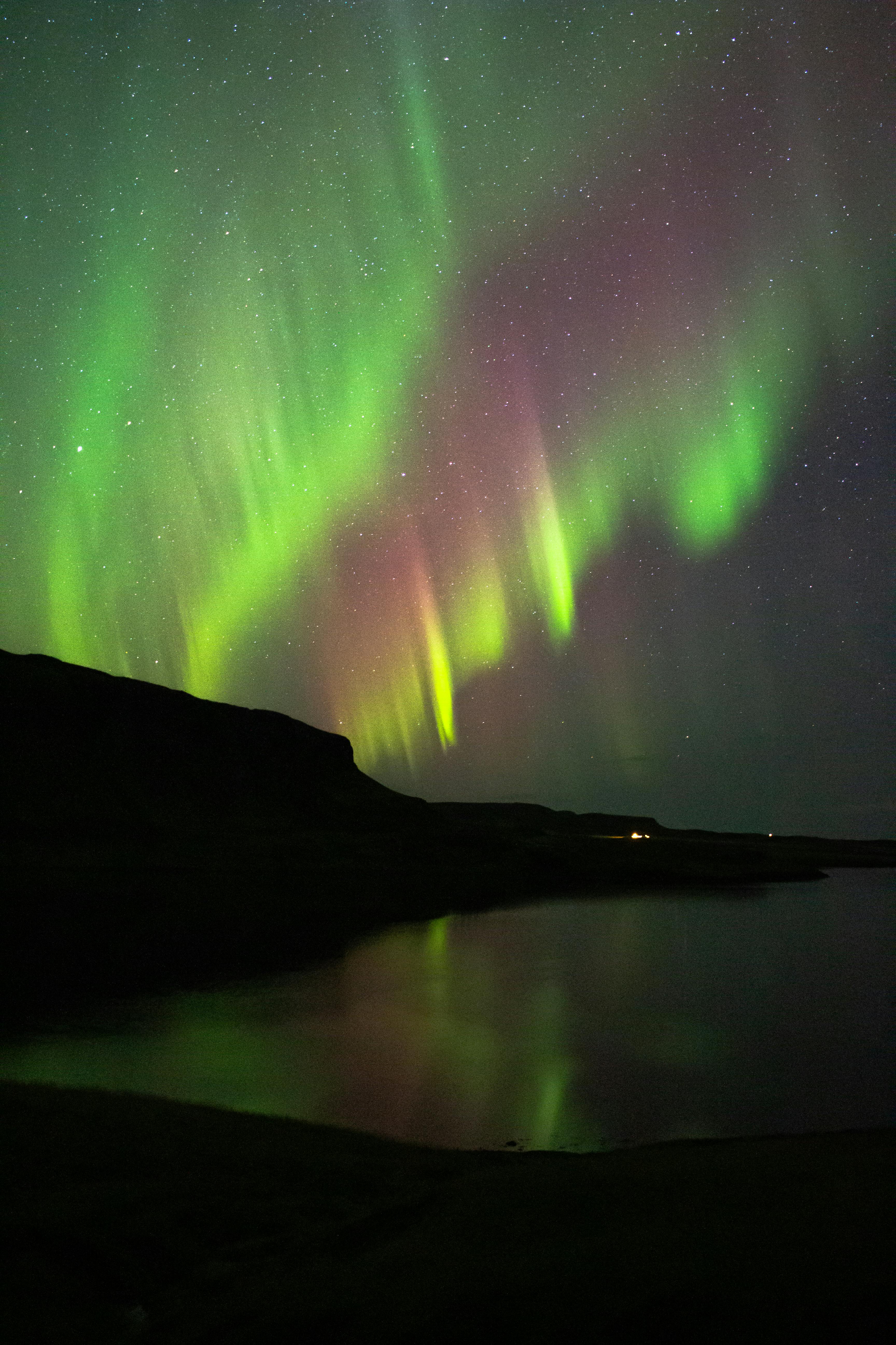 Vibrant Northern Lights illuminate the night sky over a serene Icelandic lake.