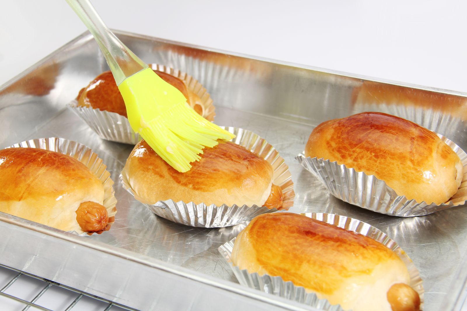Soft buns being glazed on a baking tray