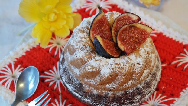 A freshly baked bundt cake topped with figs and dusted with powdered sugar, served on a vibrant red cloth with a flower for decoration.