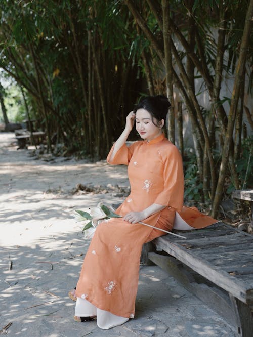 Woman in orange dress sitting on bench in park