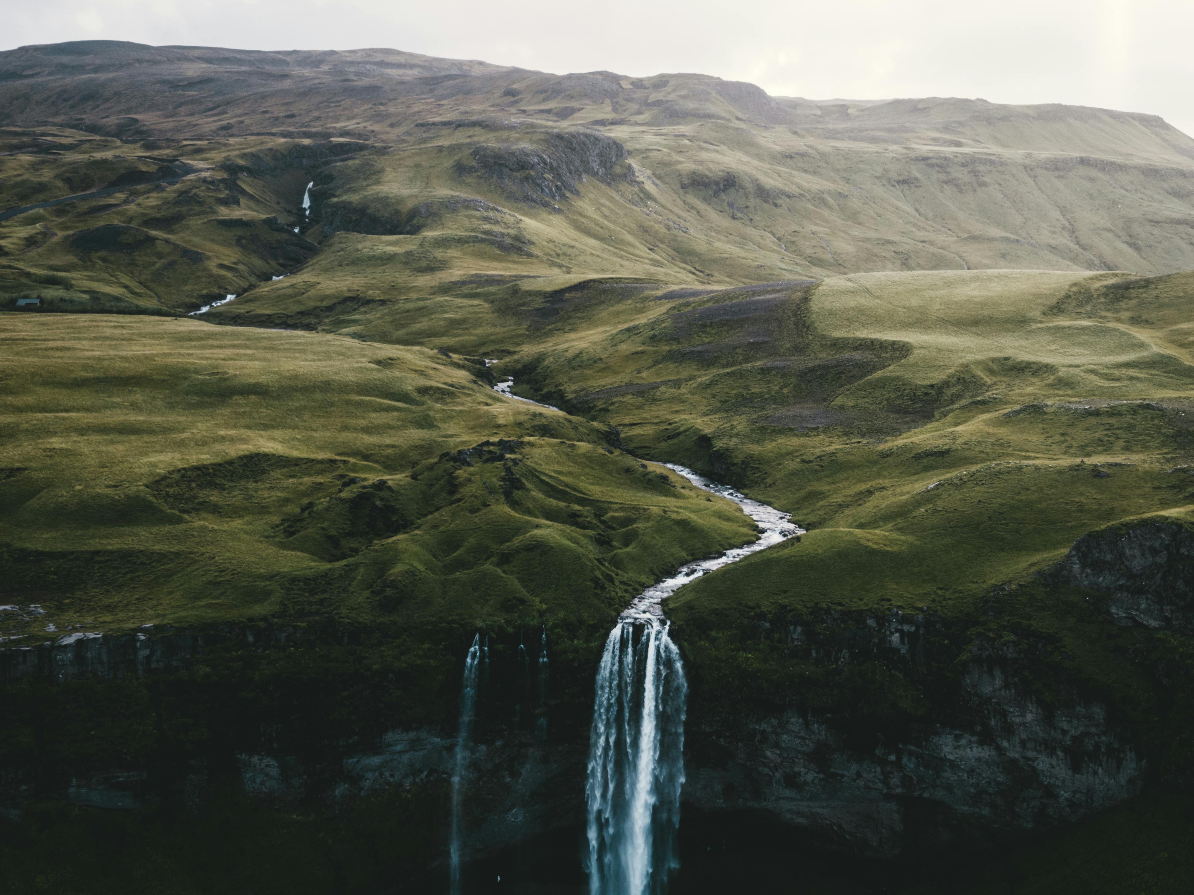 Stunning aerial view of cascading waterfall amidst Iceland's picturesque cliffs and lush terrain.