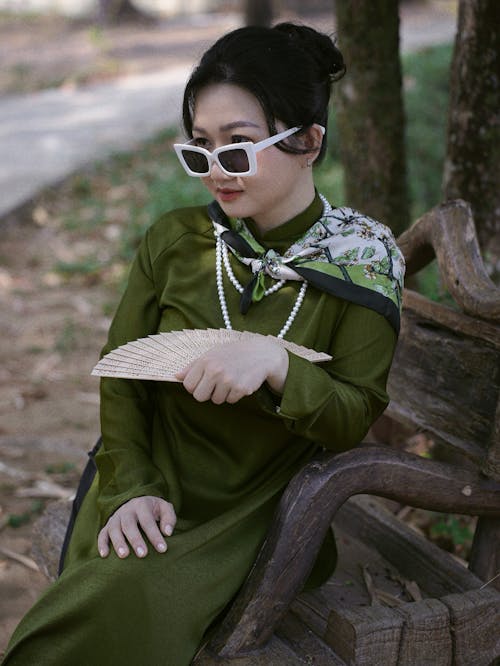 A woman in a green dress and sunglasses sitting on a bench