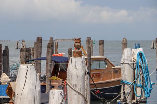 Free A scenic view of a wooden boat moored at a harbor, featuring an owl statue and wooden poles by the seaside. Stock Photo