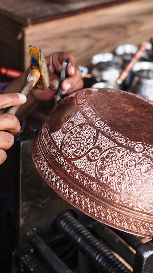 A person is working on a copper bowl