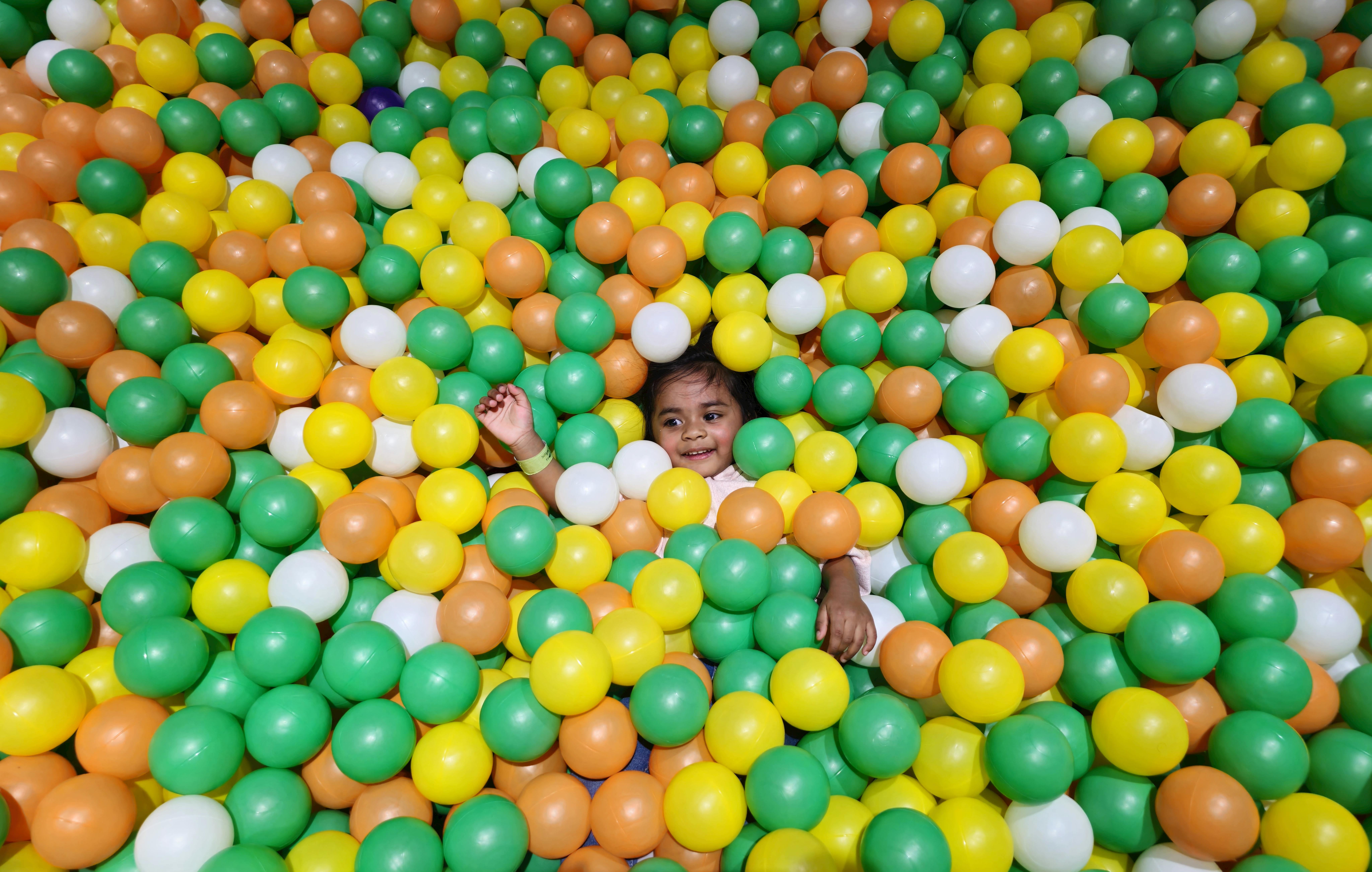 A joyful child playing and smiling amidst a vibrant ball pit filled with colorful balls.