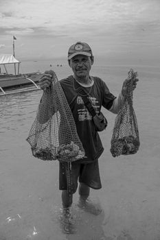 Monochrome image of an adult male fisherman standing in water holding fishing nets by the sea. - Fotografer Sidoarjo