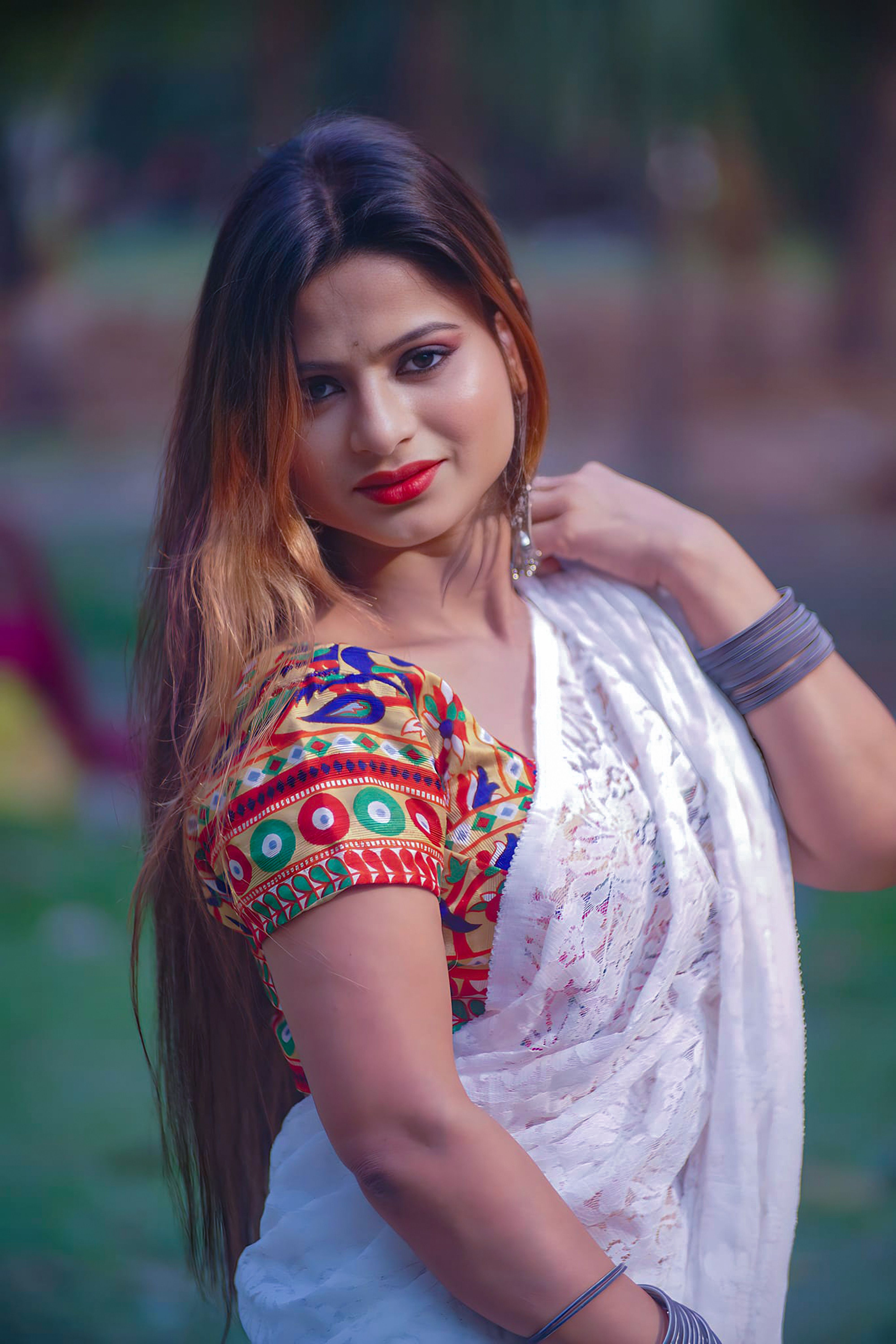 A portrait of a woman in colorful traditional Indian clothing, standing outdoors in natural light.