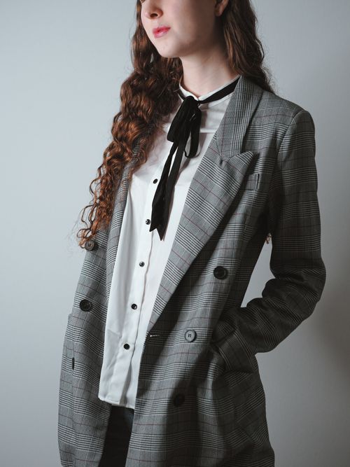 Free Portrait of a woman in a plaid blazer with a tie, set against a neutral background, exuding elegance. Stock Photo